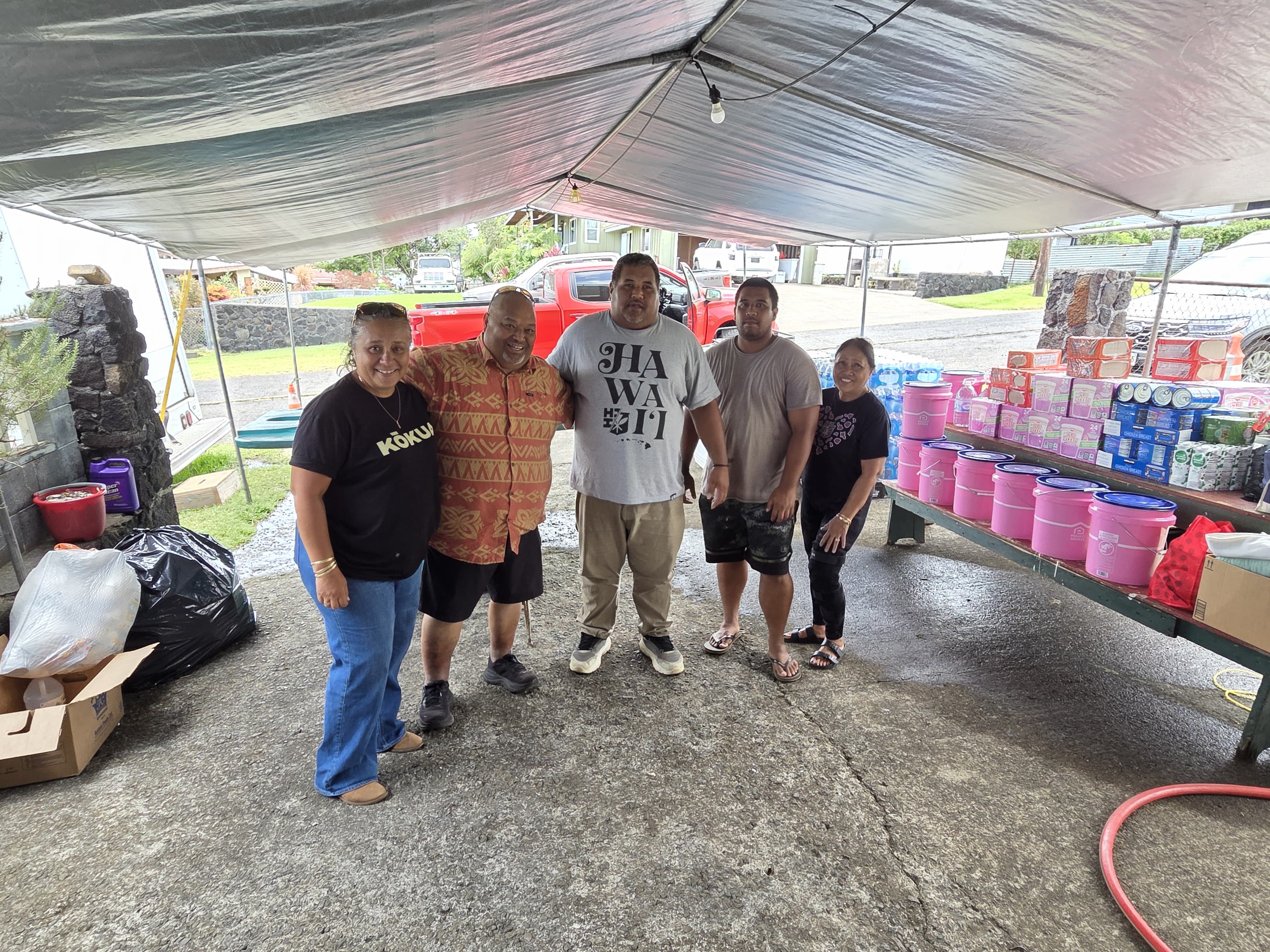 ʻOhana gathered beside donated emergency supply buckets and water at Kaumahana Hub